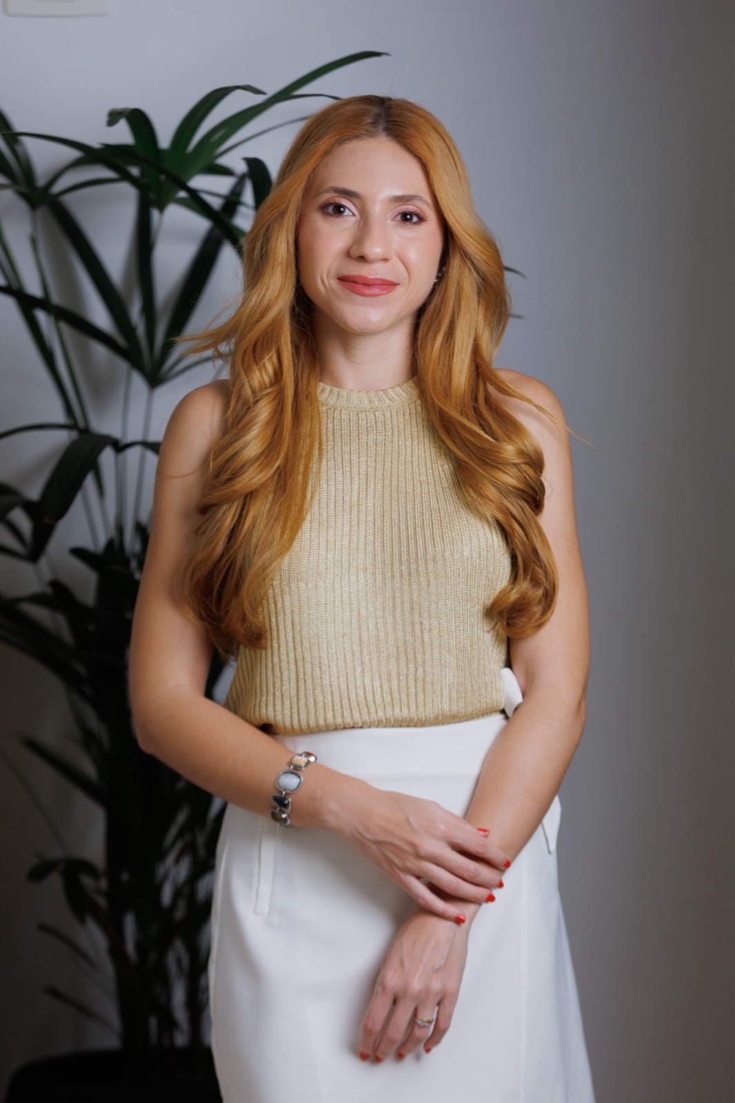 Natália Lima, psicóloga, em pé e sorrindo, com blusa bege e saia branca